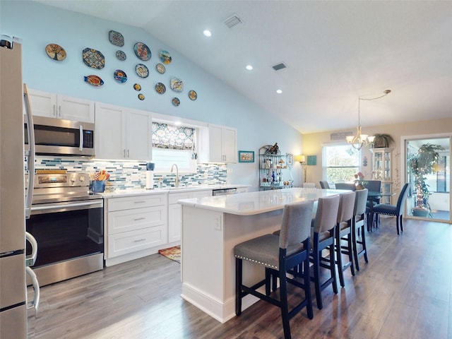 kitchen with hanging light fixtures, appliances with stainless steel finishes, wood-type flooring, and white cabinets