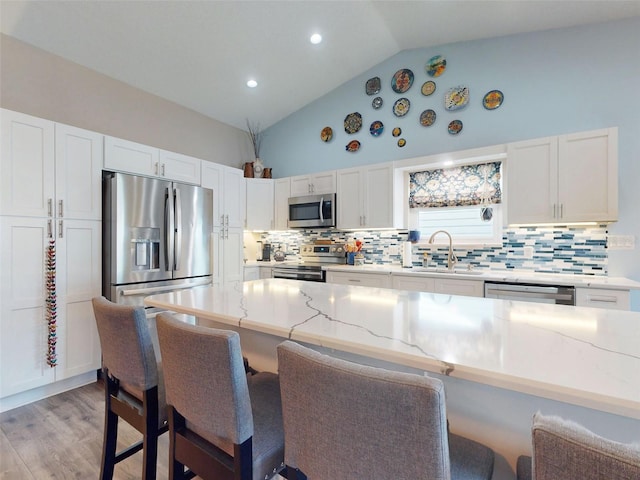 kitchen featuring stainless steel appliances, sink, vaulted ceiling, a kitchen breakfast bar, and light hardwood / wood-style flooring