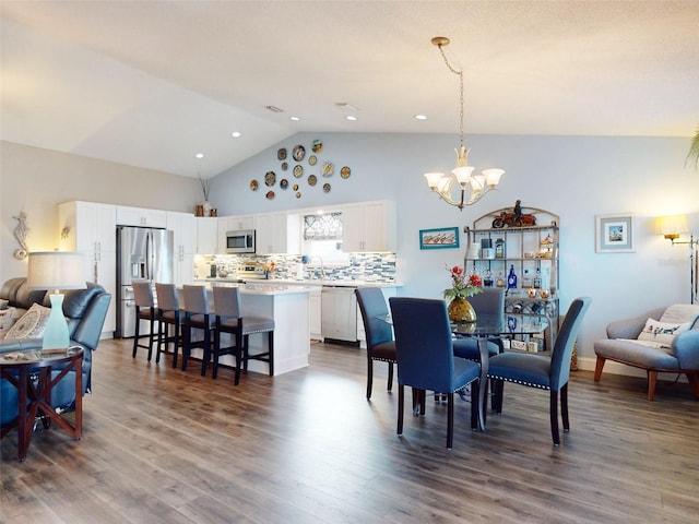 dining space featuring dark wood-type flooring, high vaulted ceiling, a chandelier, and sink