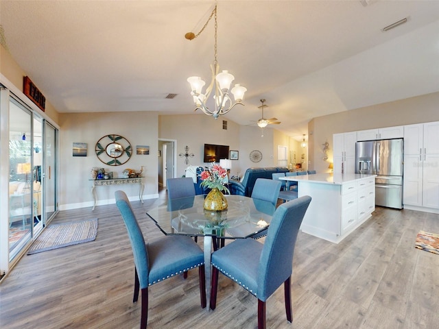 dining room featuring light wood-type flooring, ceiling fan with notable chandelier, and vaulted ceiling