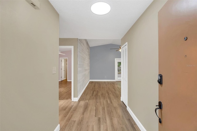 hallway featuring a textured ceiling, light hardwood / wood-style flooring, and vaulted ceiling