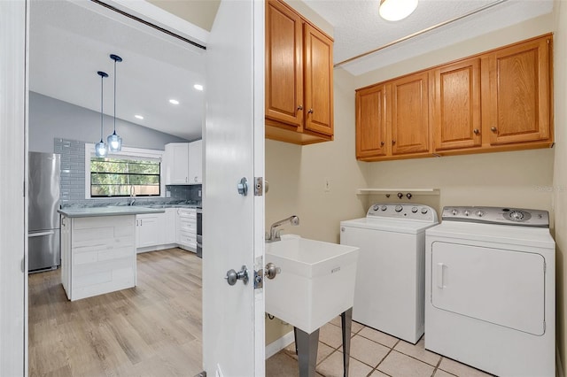 clothes washing area with cabinets, a textured ceiling, sink, washer and clothes dryer, and light hardwood / wood-style flooring