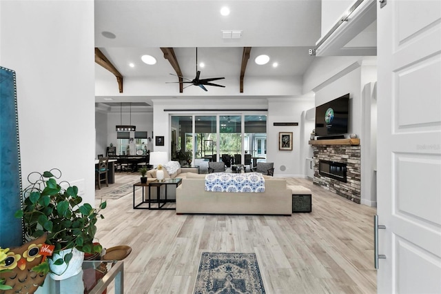 living room with beam ceiling, ceiling fan, light hardwood / wood-style floors, and a stone fireplace