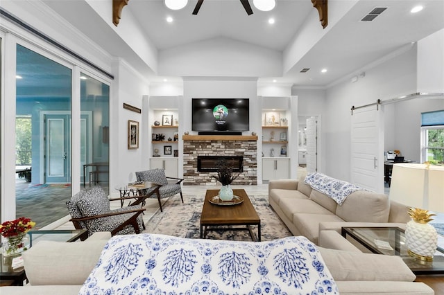 living room featuring built in shelves, ceiling fan, wood-type flooring, a barn door, and a stone fireplace