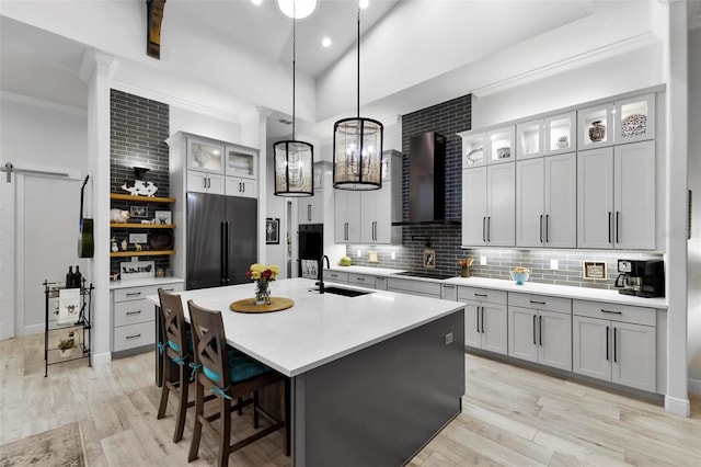 kitchen with sink, wall chimney exhaust hood, a barn door, built in fridge, and decorative light fixtures