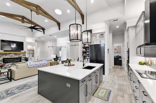 kitchen with sink, black appliances, a barn door, vaulted ceiling with beams, and an island with sink