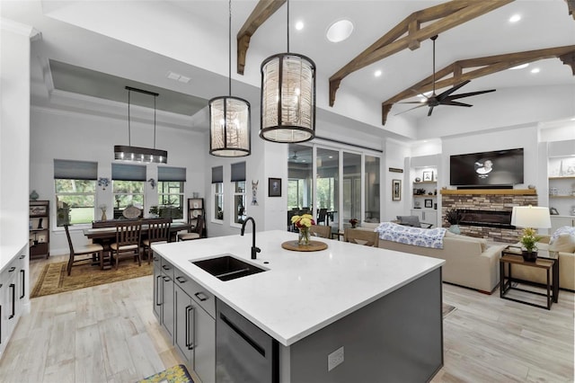 kitchen with sink, hanging light fixtures, an island with sink, stainless steel dishwasher, and light hardwood / wood-style floors