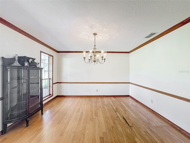 spare room with hardwood / wood-style floors, ornamental molding, a textured ceiling, and a notable chandelier