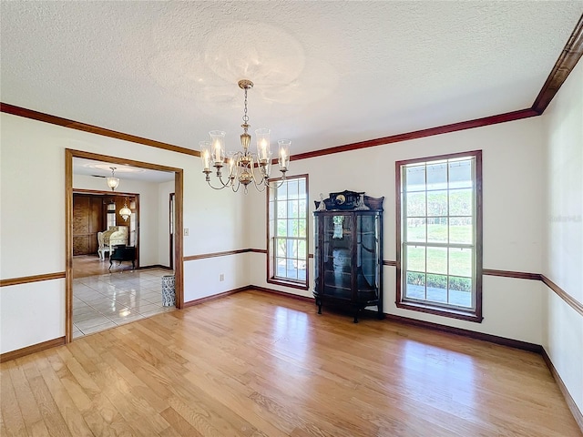 empty room featuring light hardwood / wood-style flooring, ornamental molding, a textured ceiling, and a notable chandelier