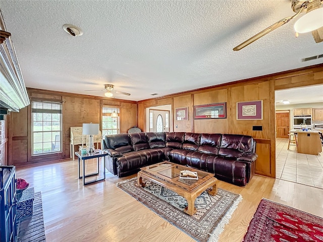 living room with a textured ceiling, light wood-type flooring, ceiling fan, and ornamental molding