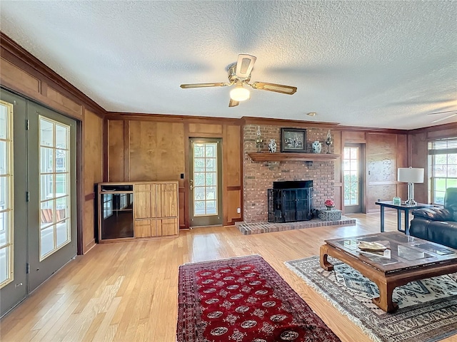 living room featuring wood walls, a brick fireplace, ceiling fan, light wood-type flooring, and a textured ceiling