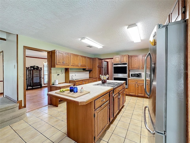 kitchen featuring tile counters, a center island, light tile patterned floors, and appliances with stainless steel finishes