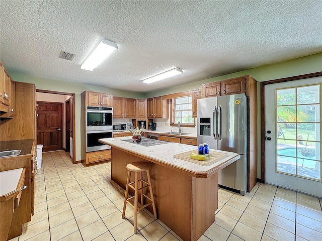 kitchen featuring tile counters, a center island, a healthy amount of sunlight, and appliances with stainless steel finishes