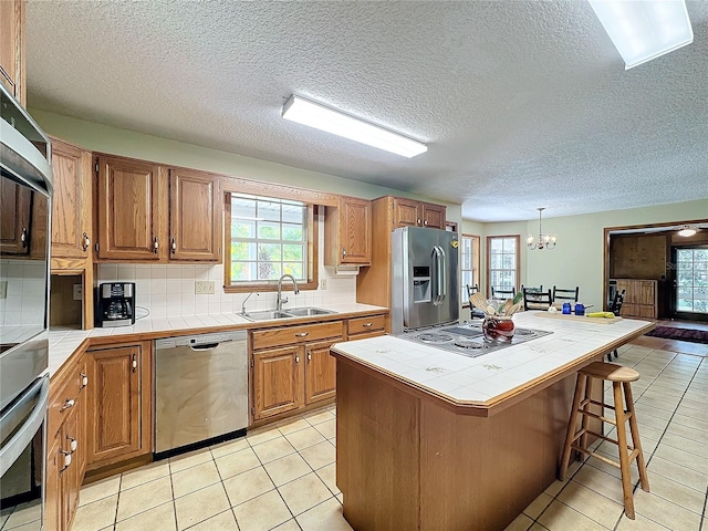 kitchen featuring tile countertops, a healthy amount of sunlight, sink, and appliances with stainless steel finishes