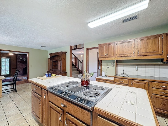 kitchen featuring tile counters, tasteful backsplash, a textured ceiling, stainless steel cooktop, and light tile patterned floors