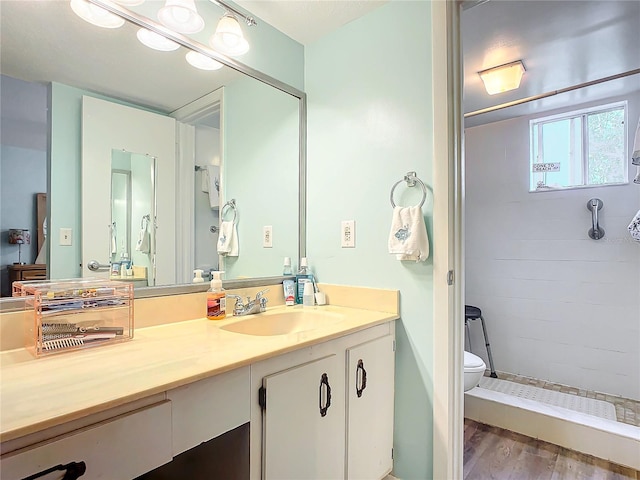 bathroom featuring toilet, vanity, hardwood / wood-style flooring, and a tile shower