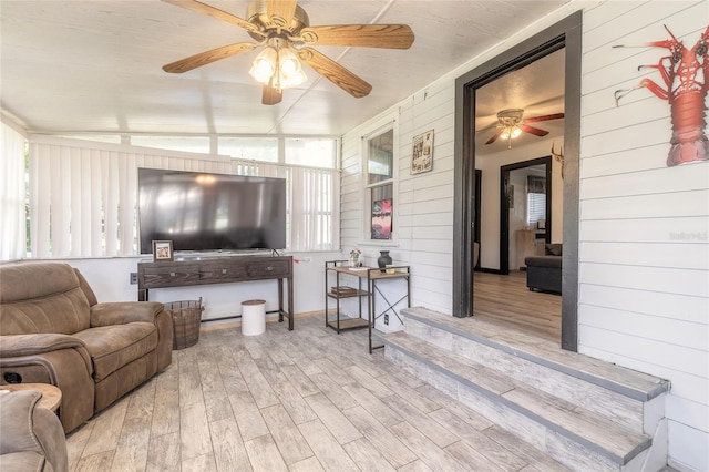 living room with ceiling fan, light hardwood / wood-style floors, lofted ceiling, and wooden walls