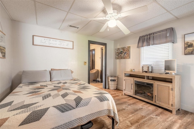 bedroom with a drop ceiling, ceiling fan, and light wood-type flooring