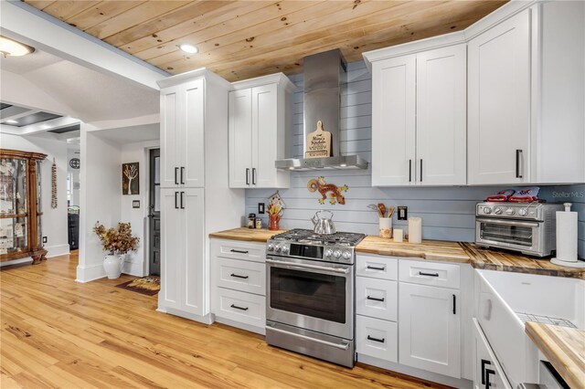 kitchen with butcher block countertops, light wood-type flooring, white cabinets, wall chimney exhaust hood, and high end range