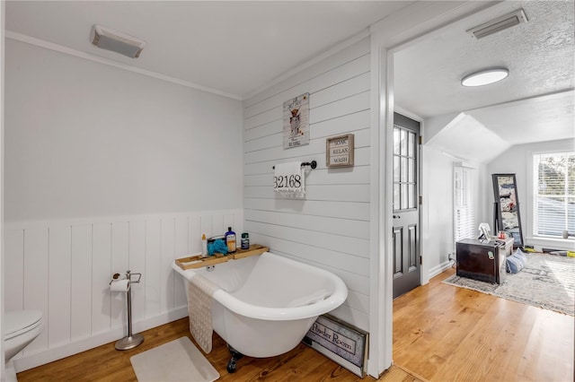 bathroom featuring wood-type flooring, toilet, wood walls, a textured ceiling, and a bath