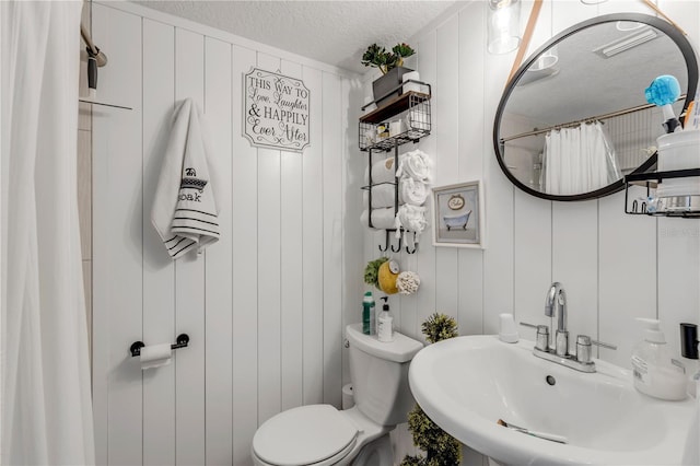 bathroom featuring sink, a shower with curtain, a textured ceiling, wooden walls, and toilet