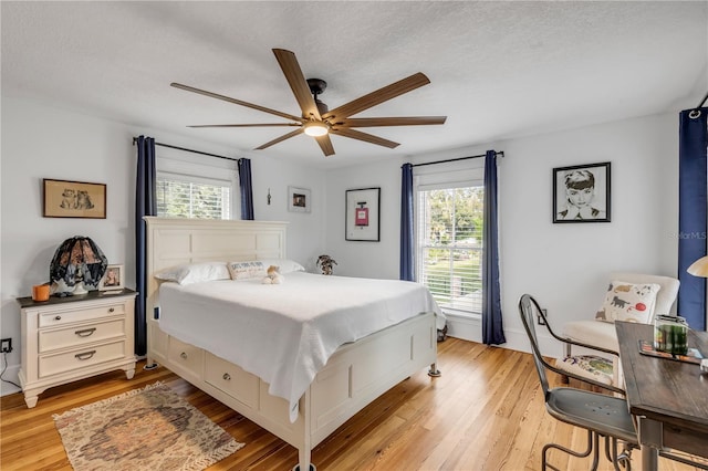 bedroom featuring ceiling fan, multiple windows, light wood-type flooring, and a textured ceiling