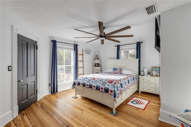 bedroom with light wood-type flooring, multiple windows, a textured ceiling, and ceiling fan