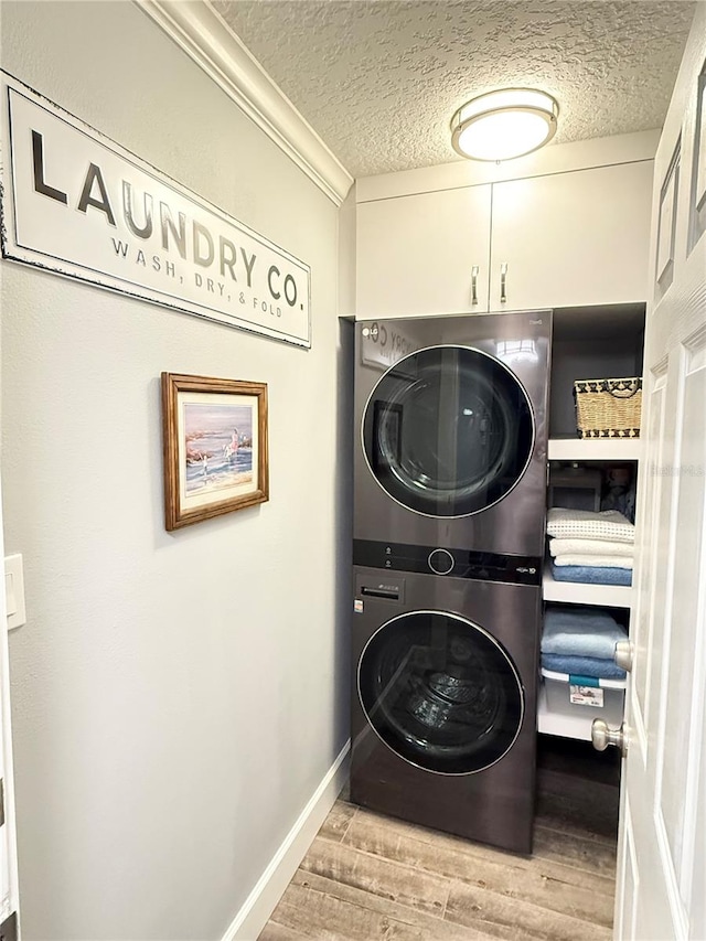 clothes washing area with cabinets, crown molding, stacked washer and dryer, light hardwood / wood-style floors, and a textured ceiling