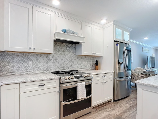 kitchen featuring light wood-type flooring, light stone counters, ornamental molding, stainless steel appliances, and white cabinetry