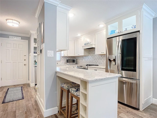 kitchen with light stone countertops, appliances with stainless steel finishes, ornamental molding, light hardwood / wood-style floors, and white cabinetry