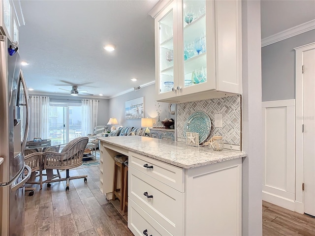 kitchen featuring light stone counters, stainless steel fridge, light hardwood / wood-style floors, white cabinets, and ornamental molding