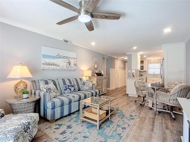 living room with ceiling fan, ornamental molding, a textured ceiling, and light wood-type flooring