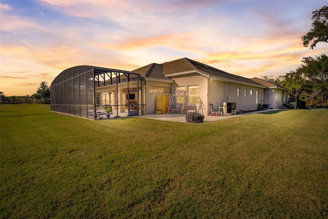 back house at dusk featuring a lawn, a lanai, and a patio