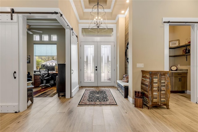 foyer featuring a towering ceiling, a barn door, a raised ceiling, light hardwood / wood-style floors, and ceiling fan with notable chandelier