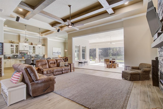 living room featuring coffered ceiling, ornamental molding, ceiling fan, beam ceiling, and light hardwood / wood-style flooring