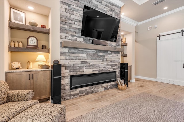 living room with a stone fireplace, light wood-type flooring, ornamental molding, and a barn door