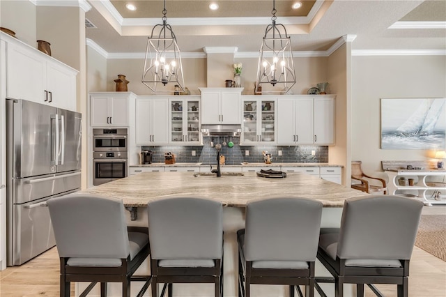 kitchen with a kitchen island with sink, stainless steel appliances, white cabinets, and a tray ceiling