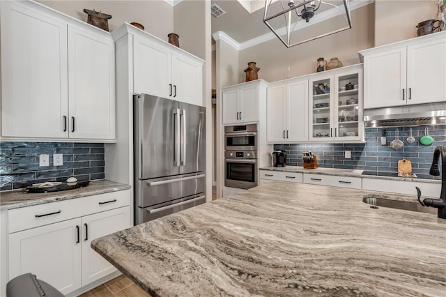 kitchen with stainless steel appliances, light stone countertops, white cabinets, and crown molding