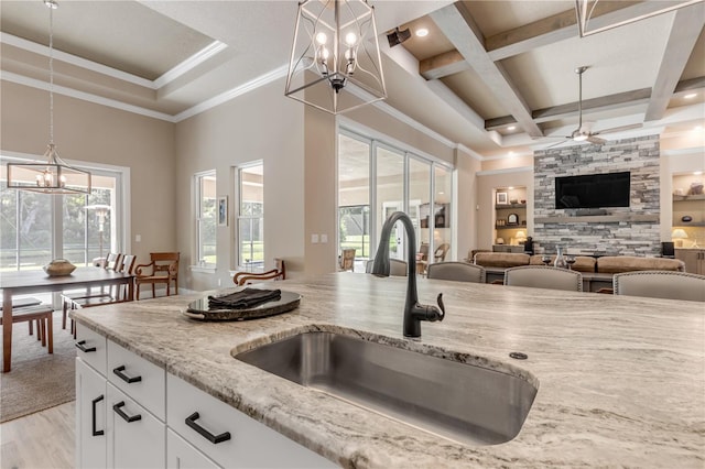 kitchen with white cabinets, sink, coffered ceiling, light stone countertops, and light wood-type flooring