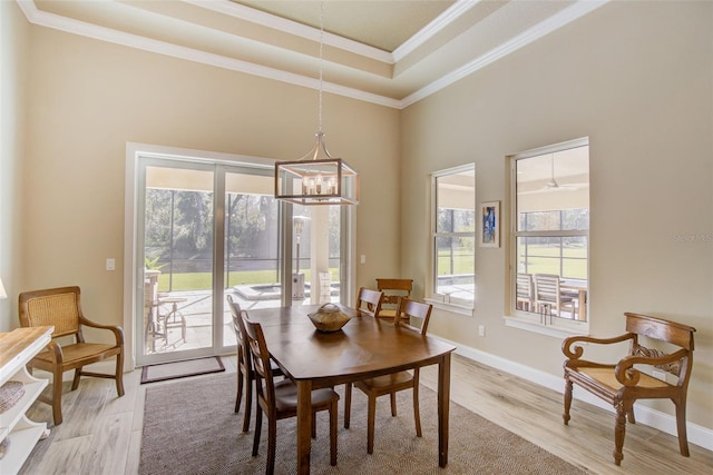 dining area featuring an inviting chandelier, a tray ceiling, light wood-type flooring, and ornamental molding