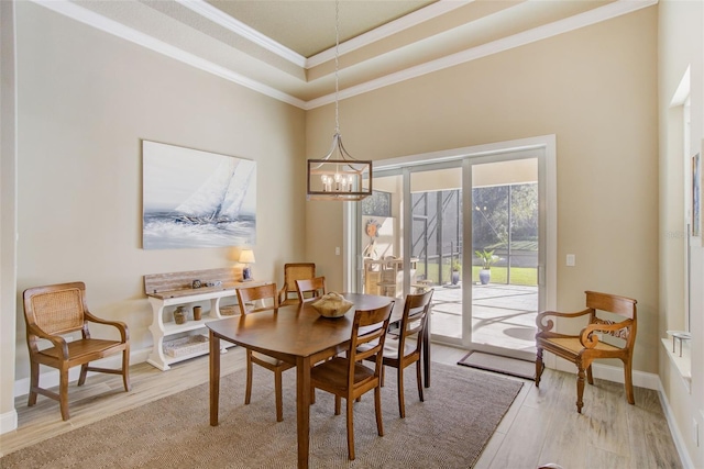 dining space with light hardwood / wood-style floors, a tray ceiling, an inviting chandelier, and ornamental molding