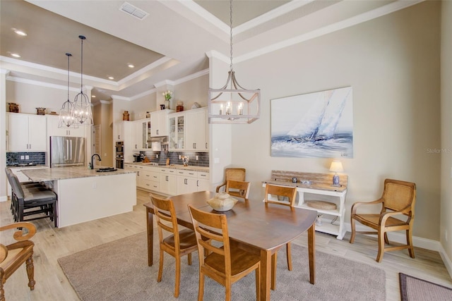 dining area with sink, a notable chandelier, light hardwood / wood-style floors, and a raised ceiling