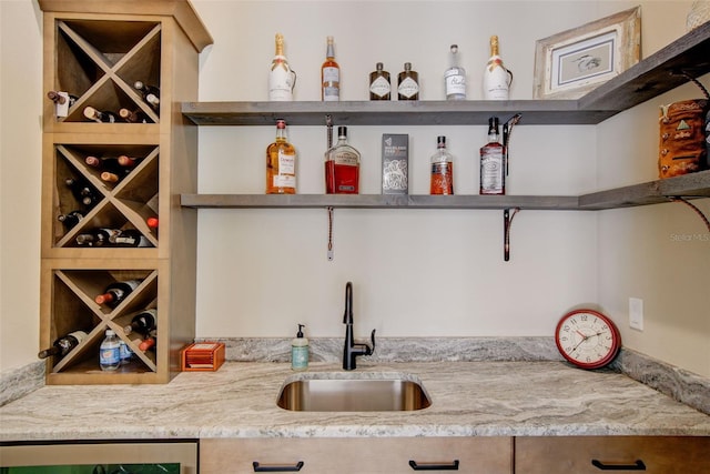 bar featuring beverage cooler, sink, and light stone counters