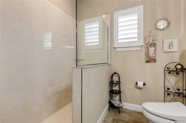 bathroom featuring toilet, wood-type flooring, and a tile shower