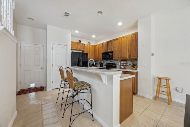 kitchen featuring a kitchen breakfast bar, tasteful backsplash, black appliances, an island with sink, and light tile patterned flooring