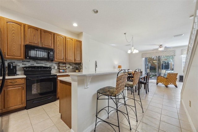 kitchen featuring light tile patterned flooring, black appliances, ceiling fan with notable chandelier, decorative backsplash, and a kitchen island