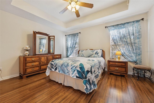 bedroom with a raised ceiling, ceiling fan, and dark hardwood / wood-style flooring