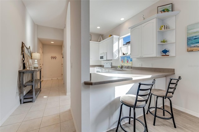 kitchen with kitchen peninsula, light tile patterned floors, a breakfast bar, white cabinetry, and white appliances