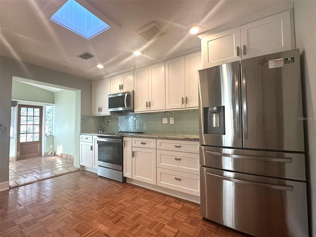 kitchen with stainless steel appliances, a skylight, white cabinets, light parquet flooring, and backsplash