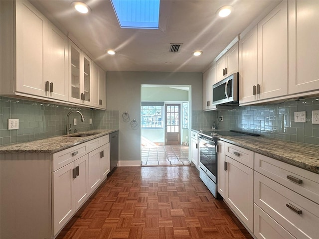 kitchen with sink, white cabinetry, light stone counters, a skylight, and appliances with stainless steel finishes